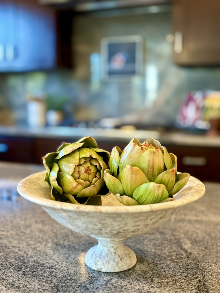 Artichokes arranged in a cream pedestal bowl in a staged kitchen