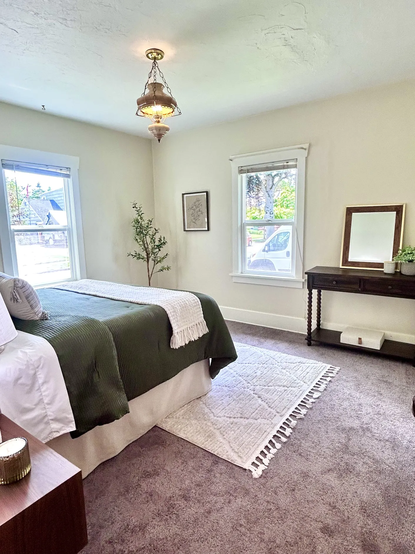 Wide view of the primary bedroom with dark green bedding and vintage ceiling light