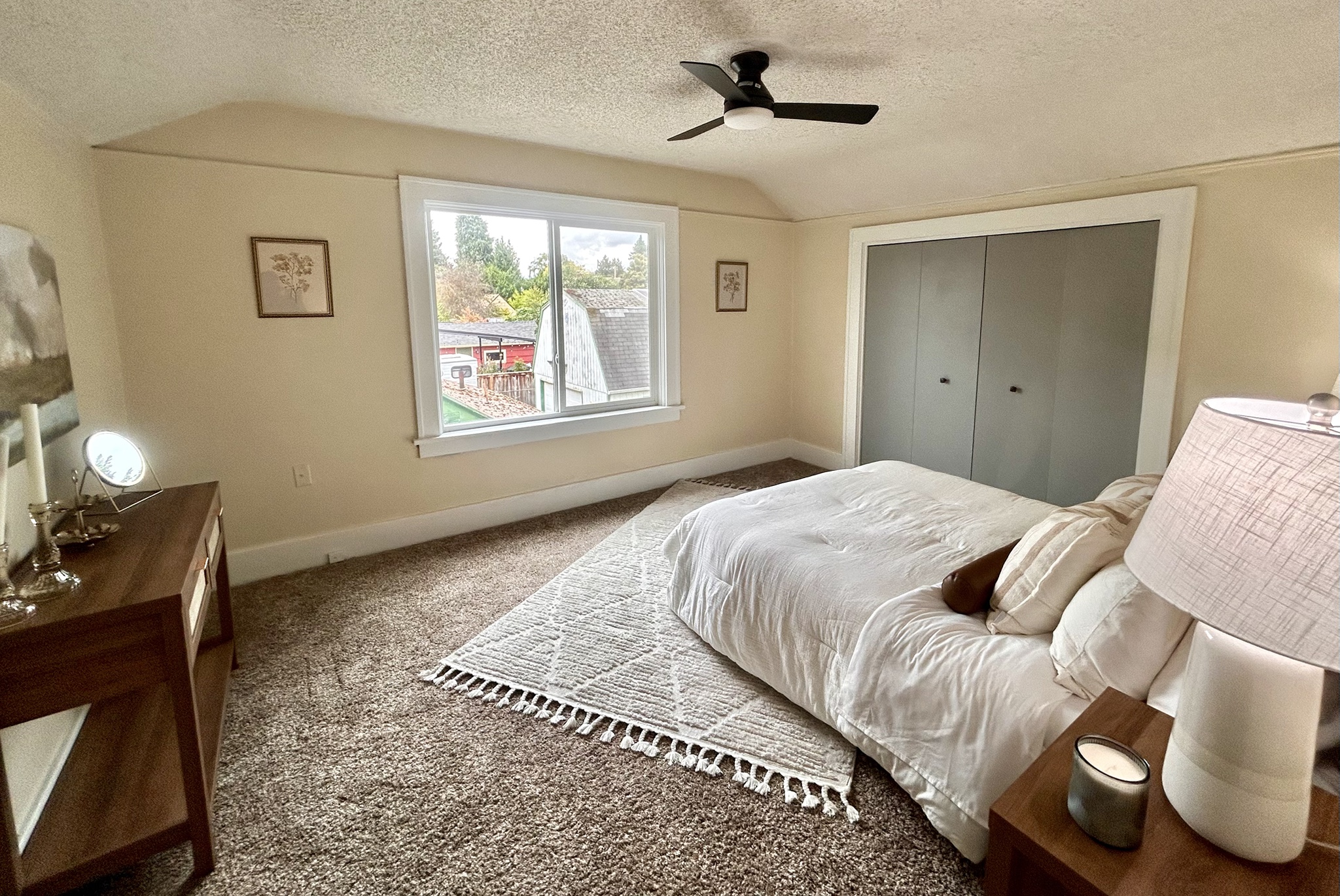 Primary bedroom with white bedding, wood furniture and a large window