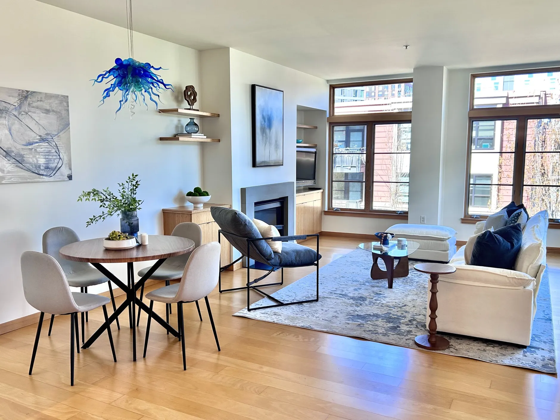 Living and dining area with white sofa, blue glass pendant, and city windows