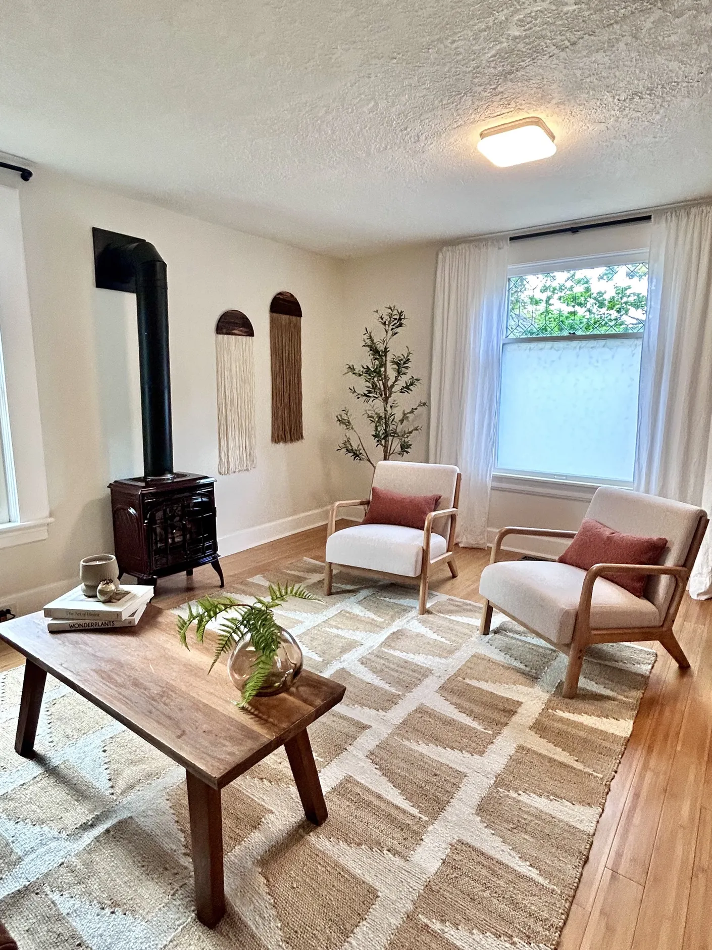 Wide view of the Sellwood living room with two cream chairs and wood stove